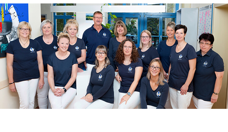 13 Personen posieren für ein Gruppenfoto in einer Praxis.