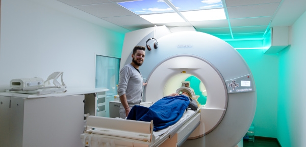 Ein Mitarbeitender steht neben einer Patienten am MRT.