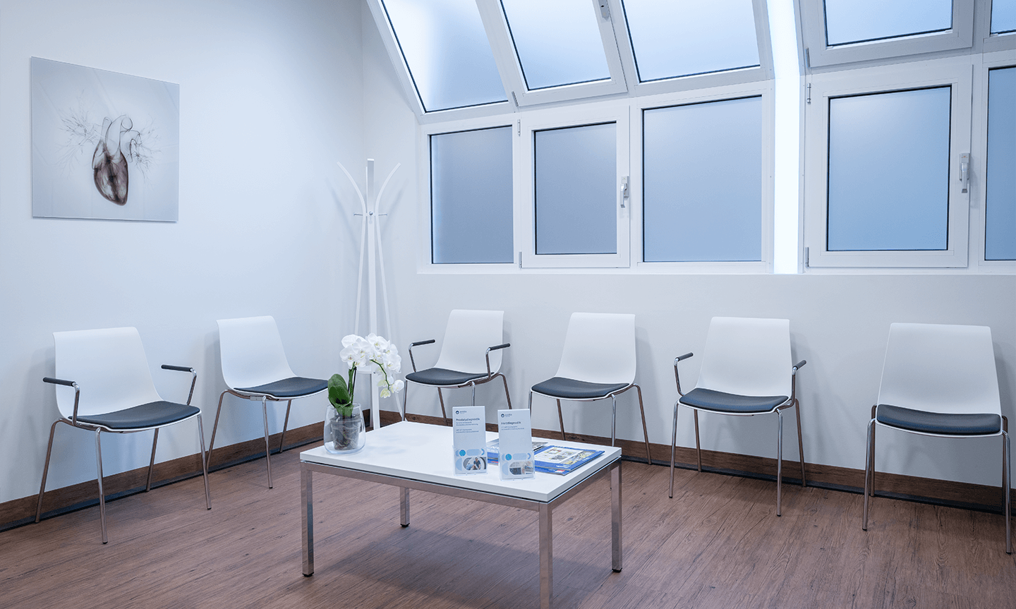 Helles Wartezimmer mit einer Reihe von weißen Stühlen und einem kleinen Tisch.
