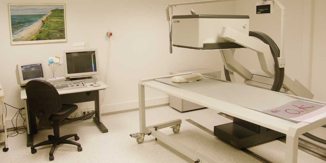 Ein weißer Raum mit einem Röntgengerät und einem Schreibtisch mit Computer.