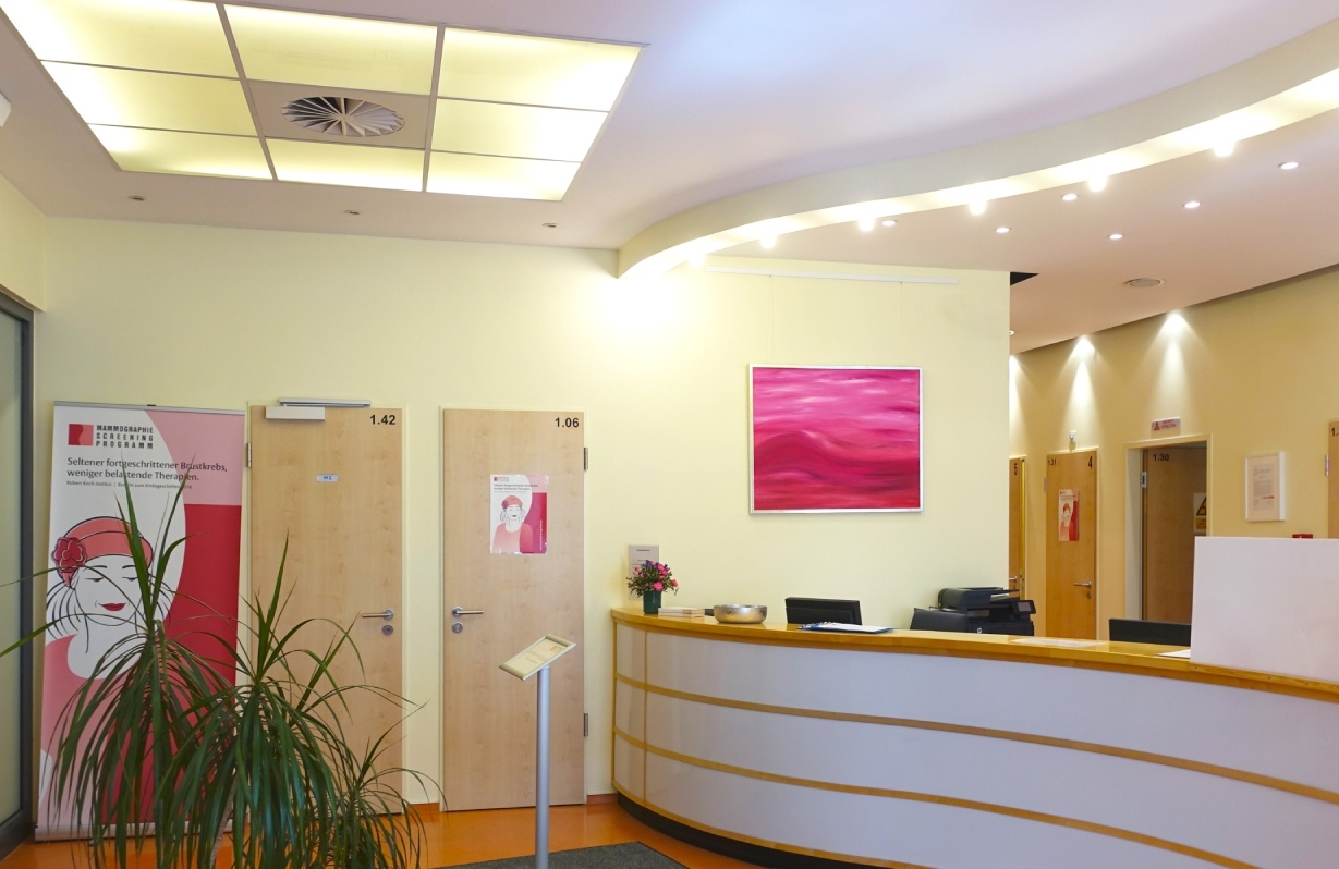 Empfangsbereich mit geschwungenem, hellen Tresen. An der Wand hängt ein abstraktes, rosa-rotes Gemälde.