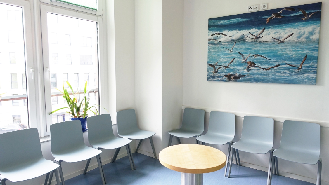 Warteecke mit hellen Wänden und blauen Boden. An der Wand ein Bild mit Meeresmotiv.