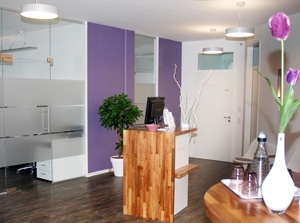 Anmeldung in der Praxis. Lila Wände und Pflanzen, Möbel hell und mit Holzoptik.