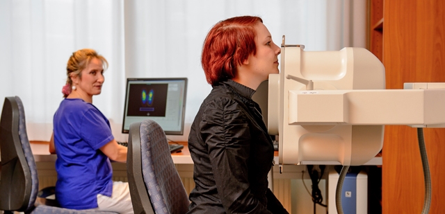 Patienten bei einer Schilddrüsenuntersuchung. Mitarbeitende sitzt im Hintergrund an einem PC.