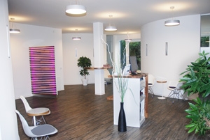 Anmeldebereich einer Praxis mit ein paar Stühlen, Pflanzen und lila Akzenten.