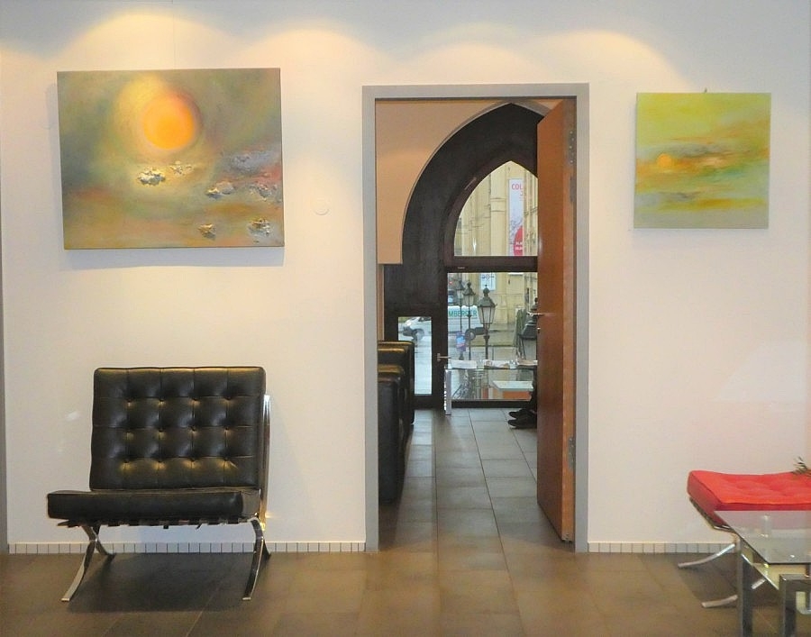 Wartezimmer mit Stühlen und Gemälde an der Wand. Blick in ein weiteres Zimmer mit großem Fenster.