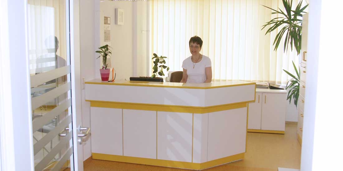 Eine Frau sitzt hinter einem Tresen zur Anmeldung in der Praxis.