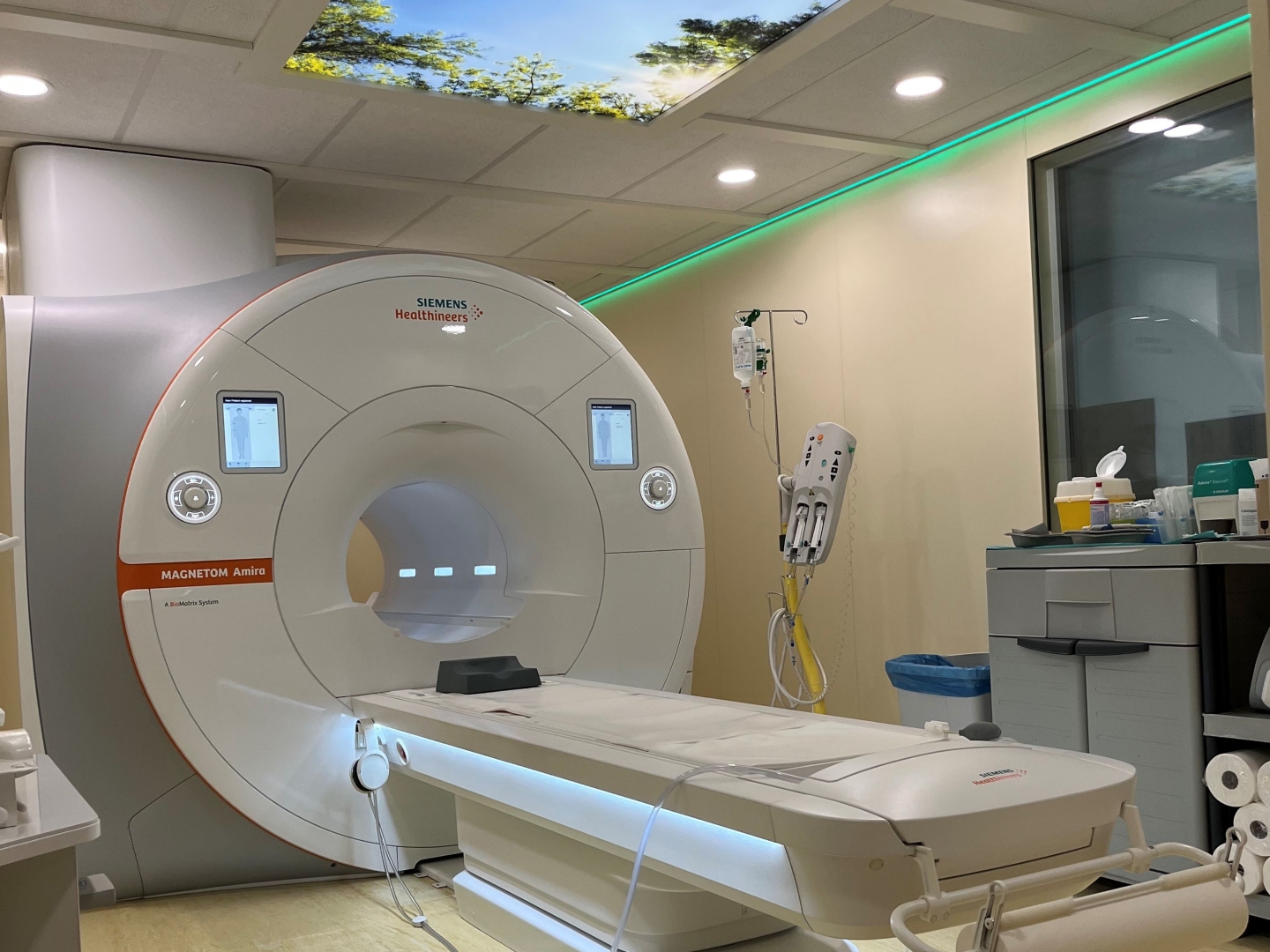 Moderner Untersuchungsraum mit einem MRT-Gerät. An der Decke befindet sich eine Lichtdecke mit Naturaufnahmen.