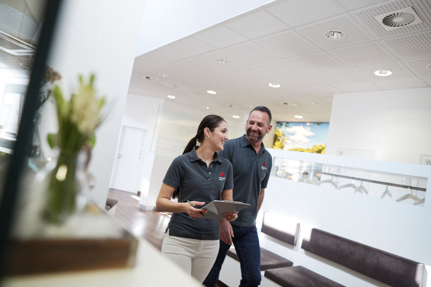 Zwei Mitarbeitende gehen durch ein helles Wartezimmer und lächeln dabei