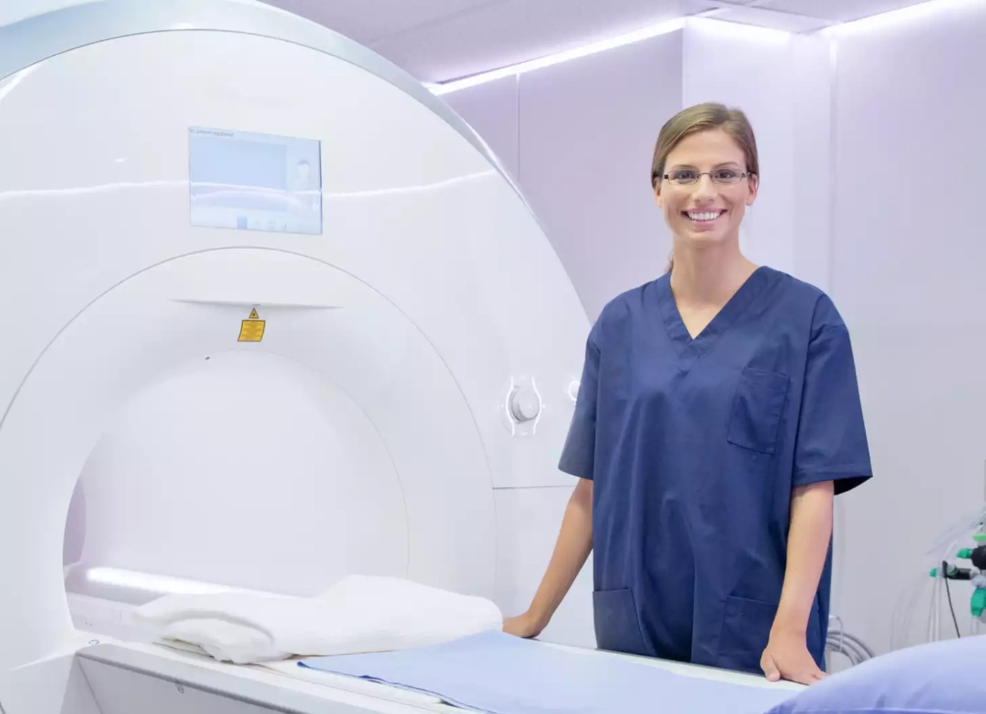 Eine medizinische Fachangestellte steht vor einem MRT-Scanner