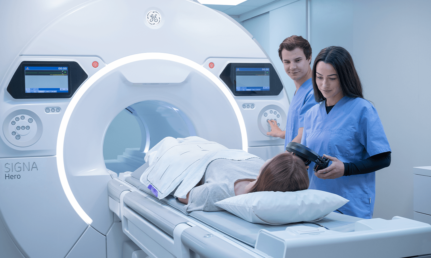Zwei MFA arbeiten am einem MRT-Gerät. Ein Patient liegt auf einer Liege.