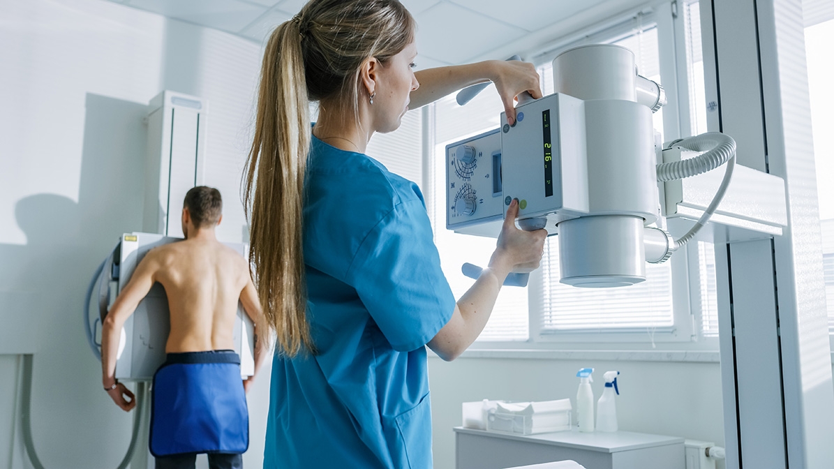 Ärztin arbeitet an einem radiologischen Gerät, welches einen Patienten untersucht.