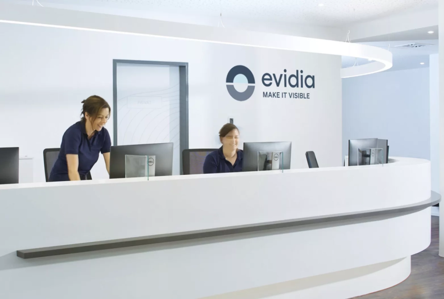 Zwei medizinische Fachangestellte arbeiten am Empfang, das evidia Logo ist an der Wand zu sehen
