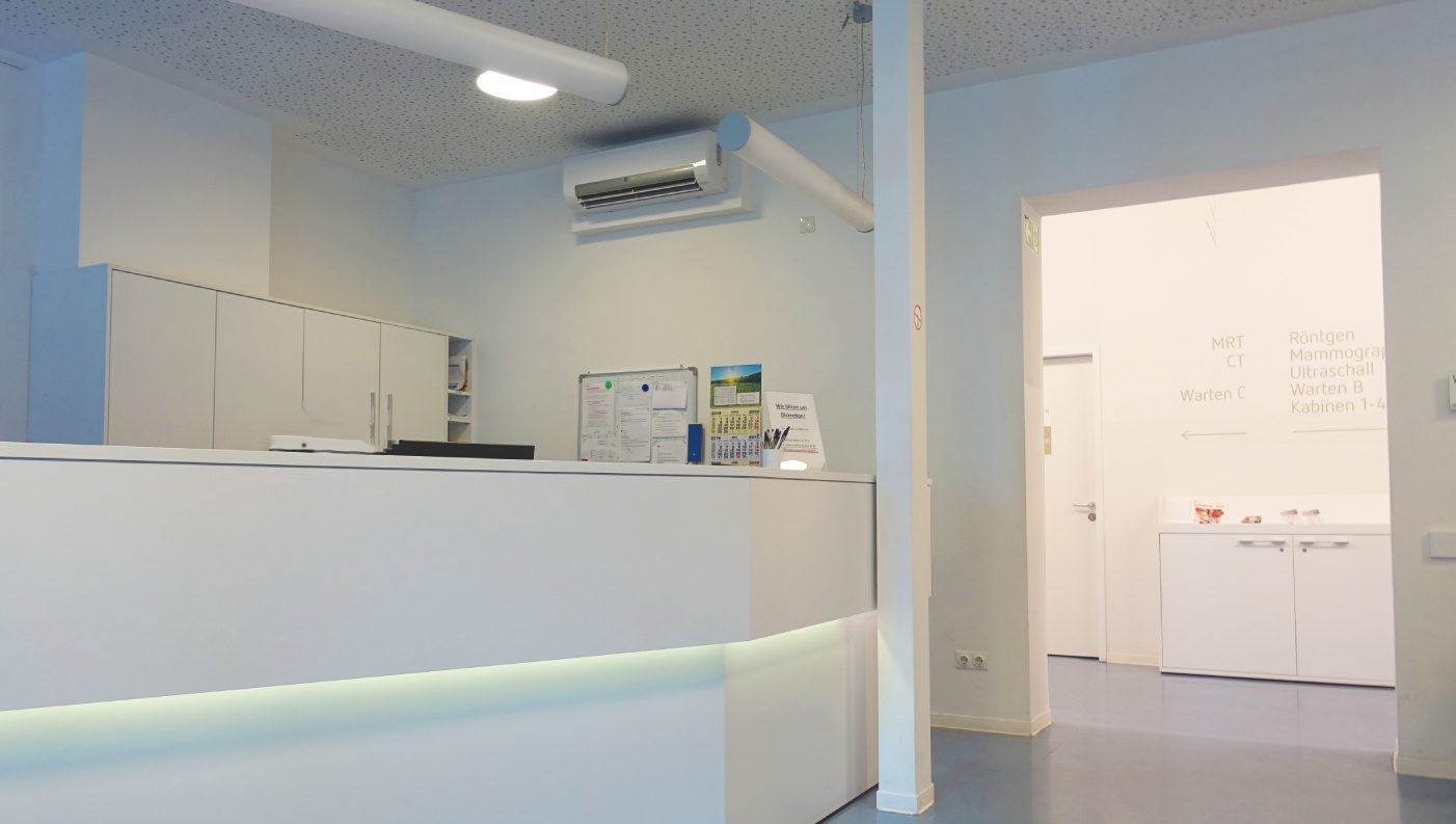 Weißer Empfangstresen mit Lichtstreifen in einer modernen, hellen Praxis. Im Hintergrund sind nach der Türöffnung die Richtung der verschiedenen Bereiche angezeigt.